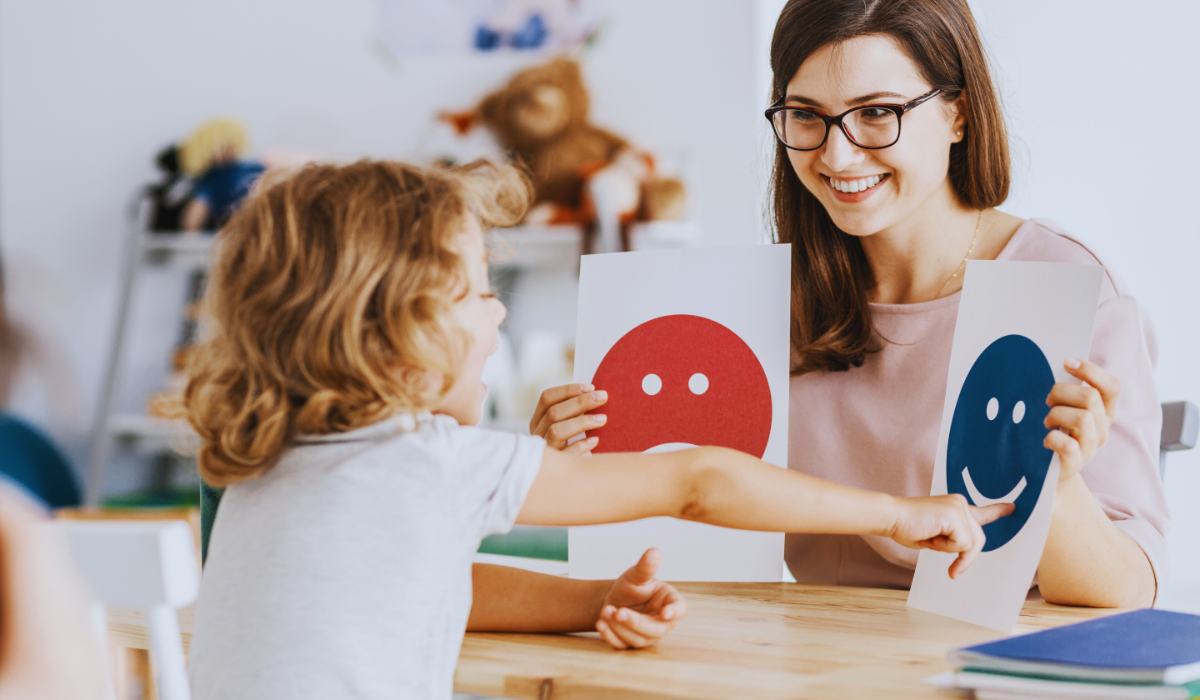 A woman holding a happy and sad face papers to a child