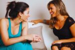 two female friends sitting on a sofa and talking