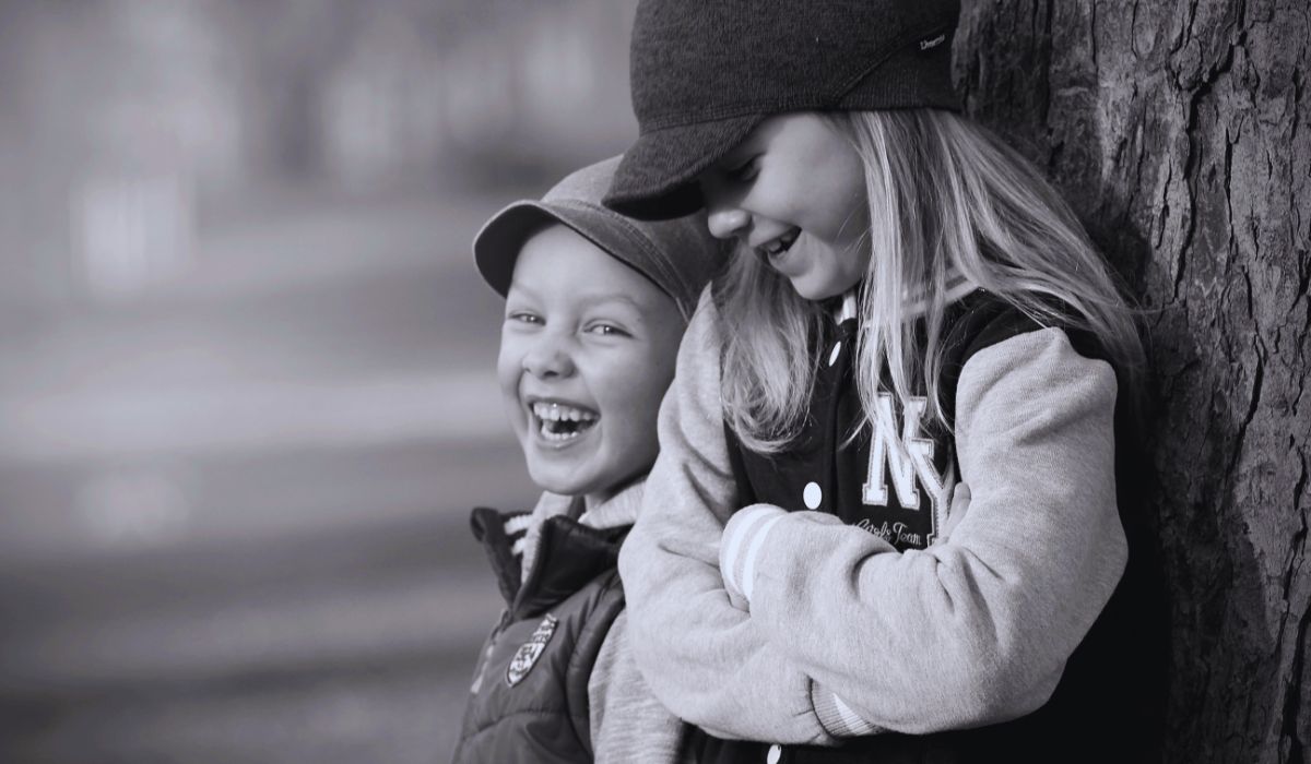 A brother and sister laughing against a tree