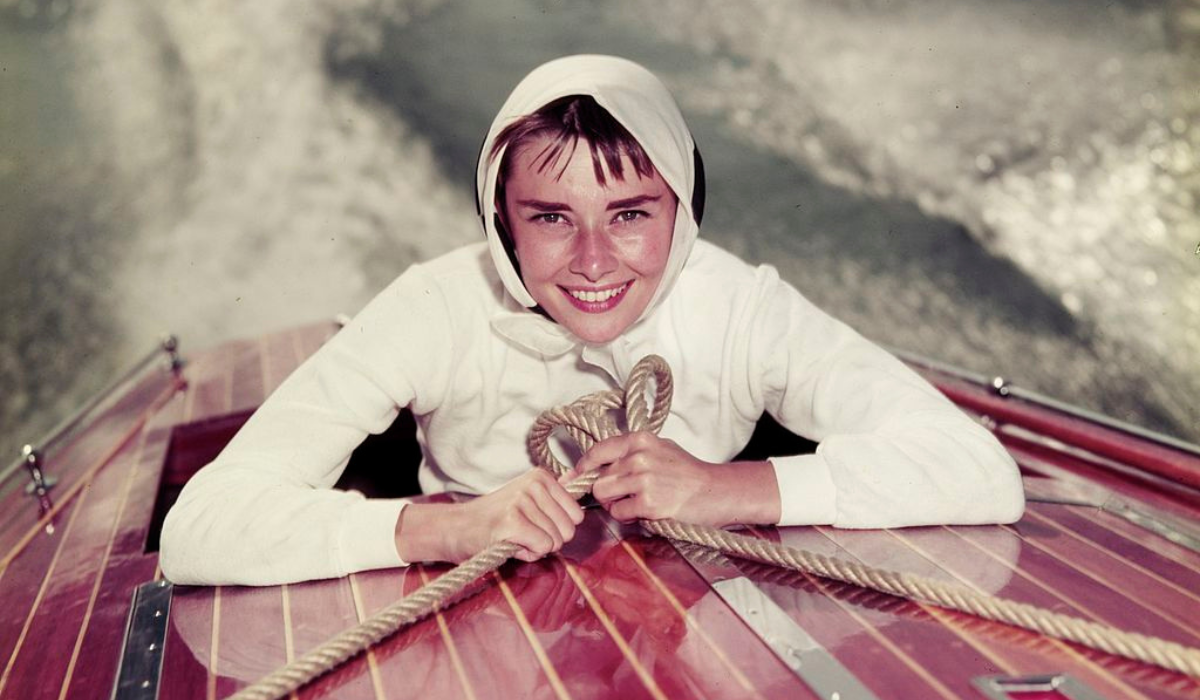 Audrey Hepburn posing in a read boat on the water