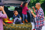 a family of four standing behind their car