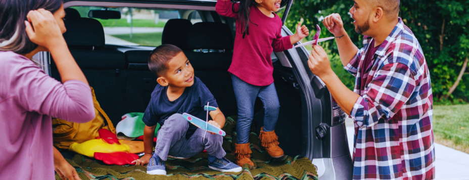 a family of four standing behind their car