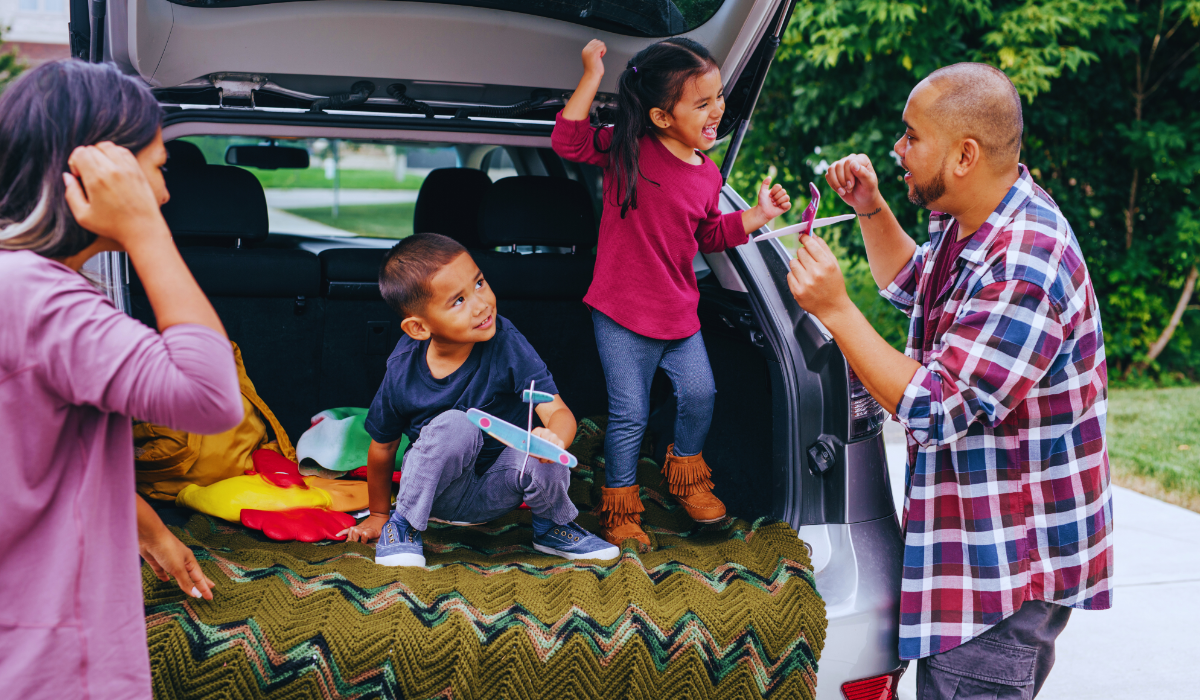 a family of four standing behind their car