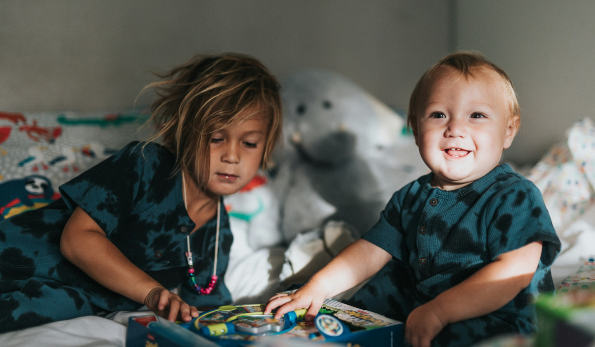 Two young siblings playing on a bed